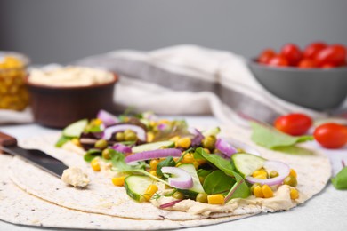 Tortilla with hummus and vegetables on table, closeup