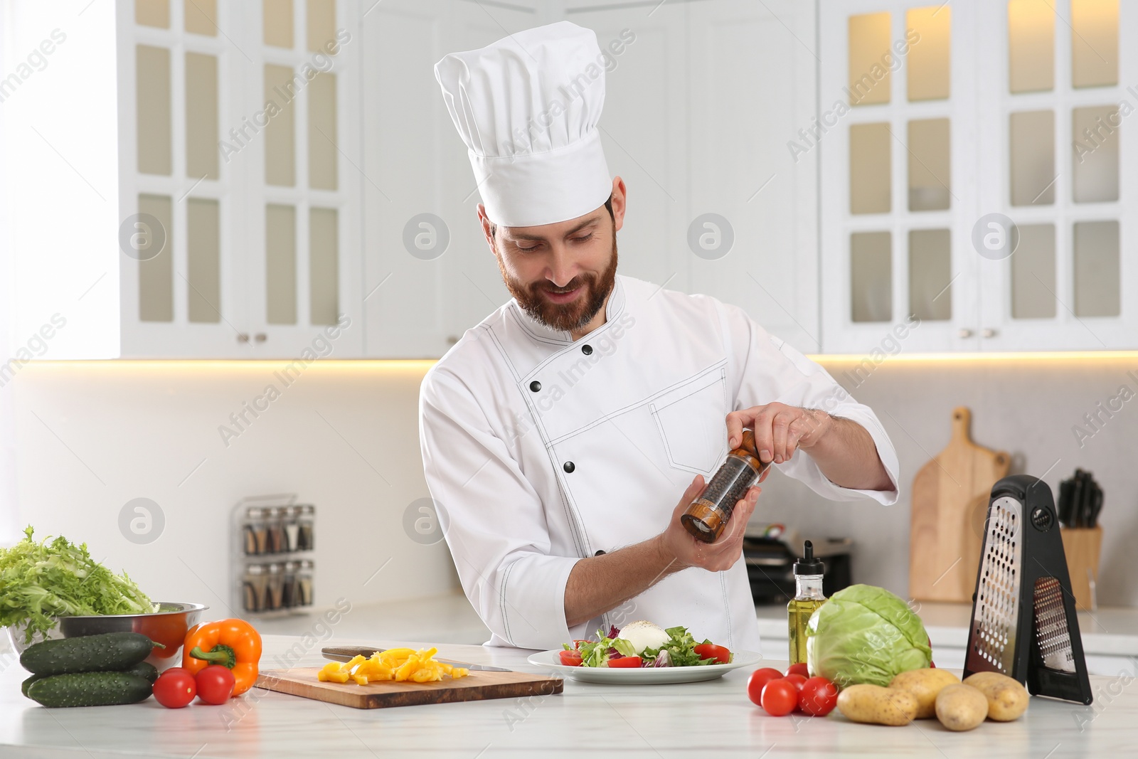 Photo of Professional chef adding pepper into delicious salad at marble table in kitchen