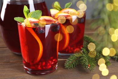 Photo of Aromatic Christmas Sangria drink and fir branches on wooden table, closeup