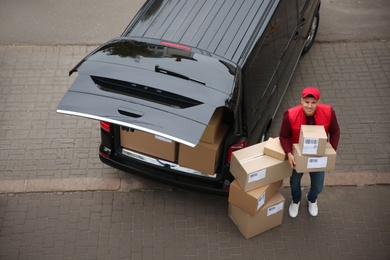 Photo of Courier with parcels near delivery van outdoors, above view