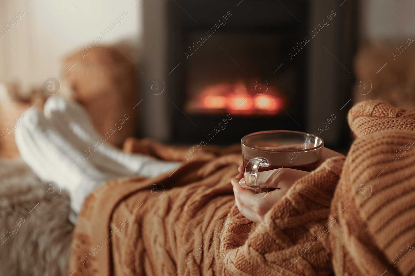 Photo of Woman with cup of tea resting near fireplace at home, closeup