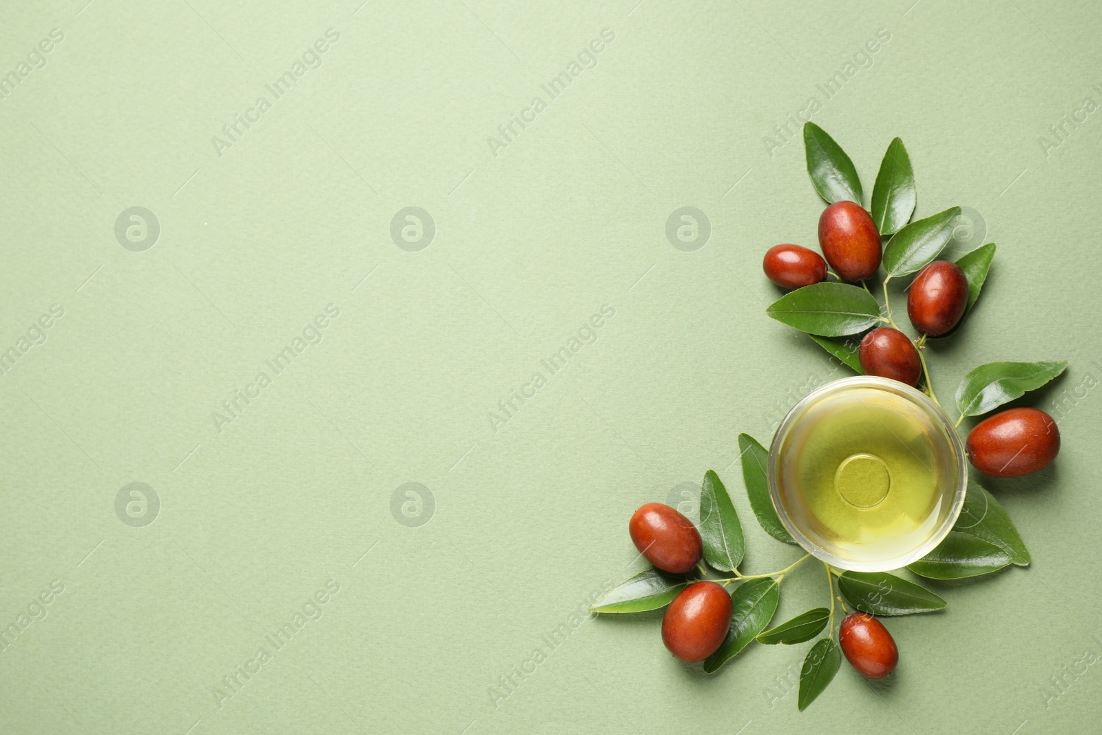 Photo of Glass bowl with jojoba oil and seeds on green background, flat lay. Space for text