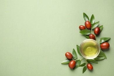 Glass bowl with jojoba oil and seeds on green background, flat lay. Space for text