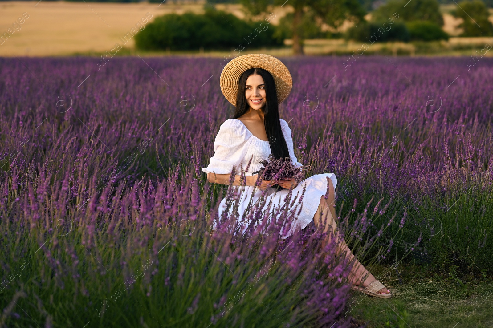 Photo of Beautiful young woman with bouquet sitting in lavender field