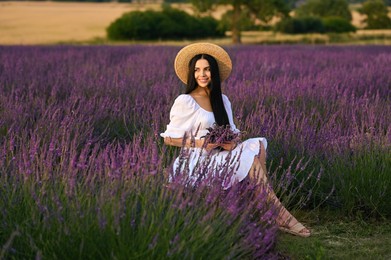 Beautiful young woman with bouquet sitting in lavender field