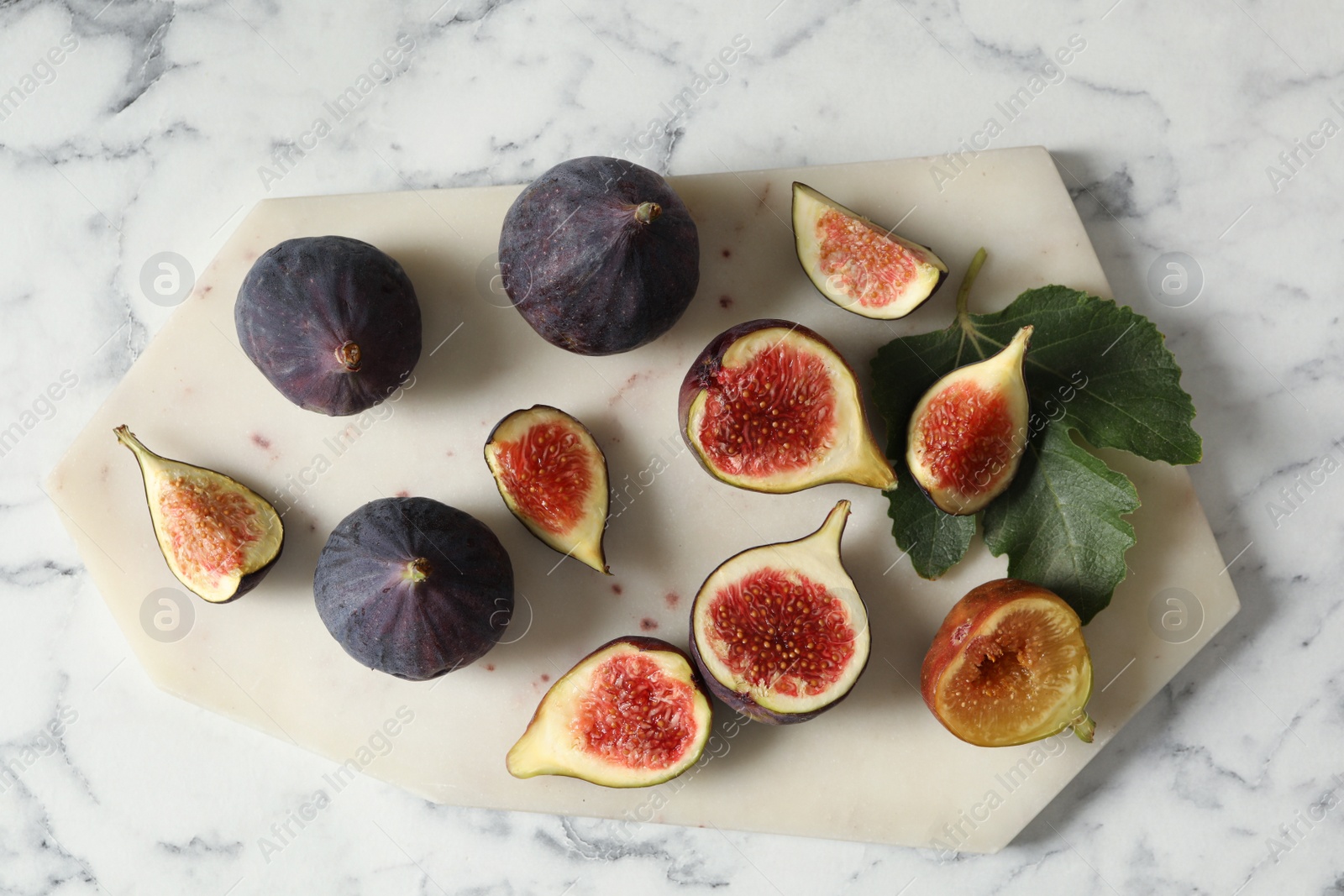 Photo of Whole and cut tasty fresh figs with green leaf on white marble table, flat lay