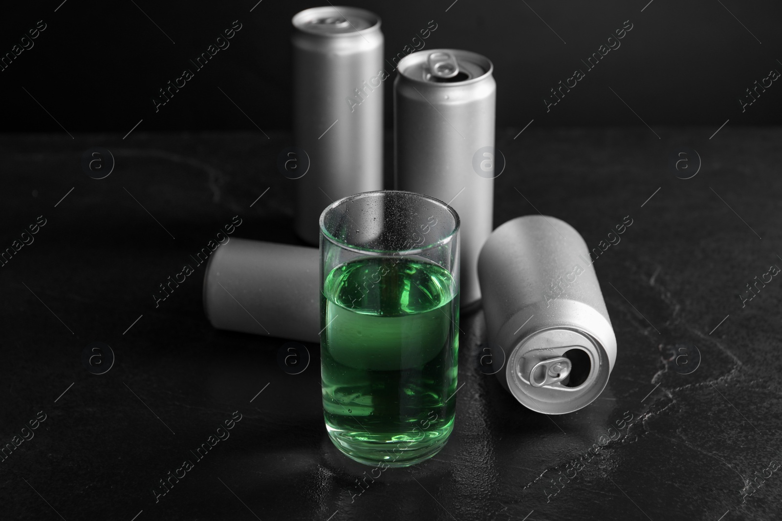 Photo of Energy drink in glass and aluminium cans on black table