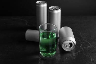 Photo of Energy drink in glass and aluminium cans on black table