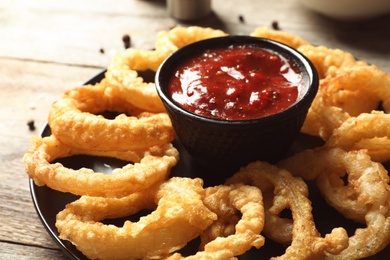 Photo of Homemade crunchy fried onion rings with tomato sauce on wooden table, closeup