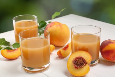 Photo of Glasses of peach juice, fresh fruits and leaves on white wooden table