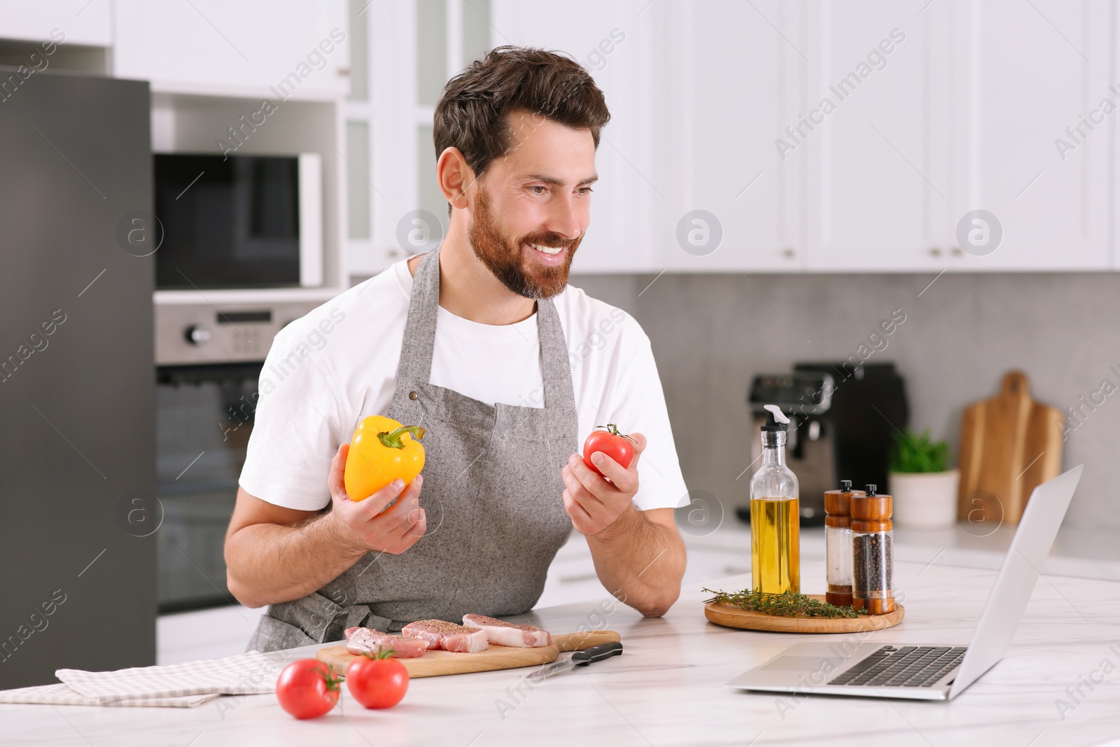 Photo of Man making dinner while watching online cooking course via laptop in kitchen