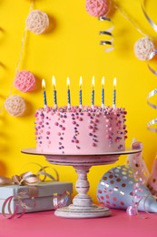 Photo of Delicious birthday cake and party decor on pink table against yellow background