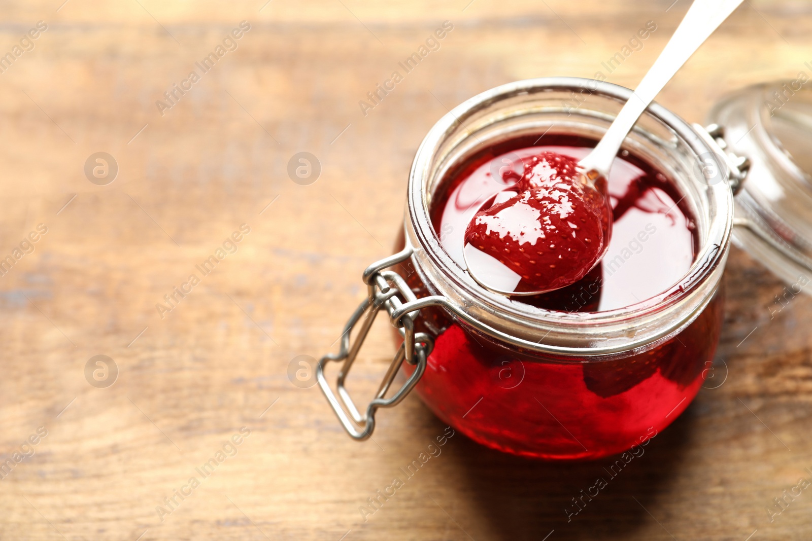 Photo of Delicious pickled strawberry jam in glass jar on wooden table, closeup. Space for text