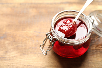 Photo of Delicious pickled strawberry jam in glass jar on wooden table, closeup. Space for text
