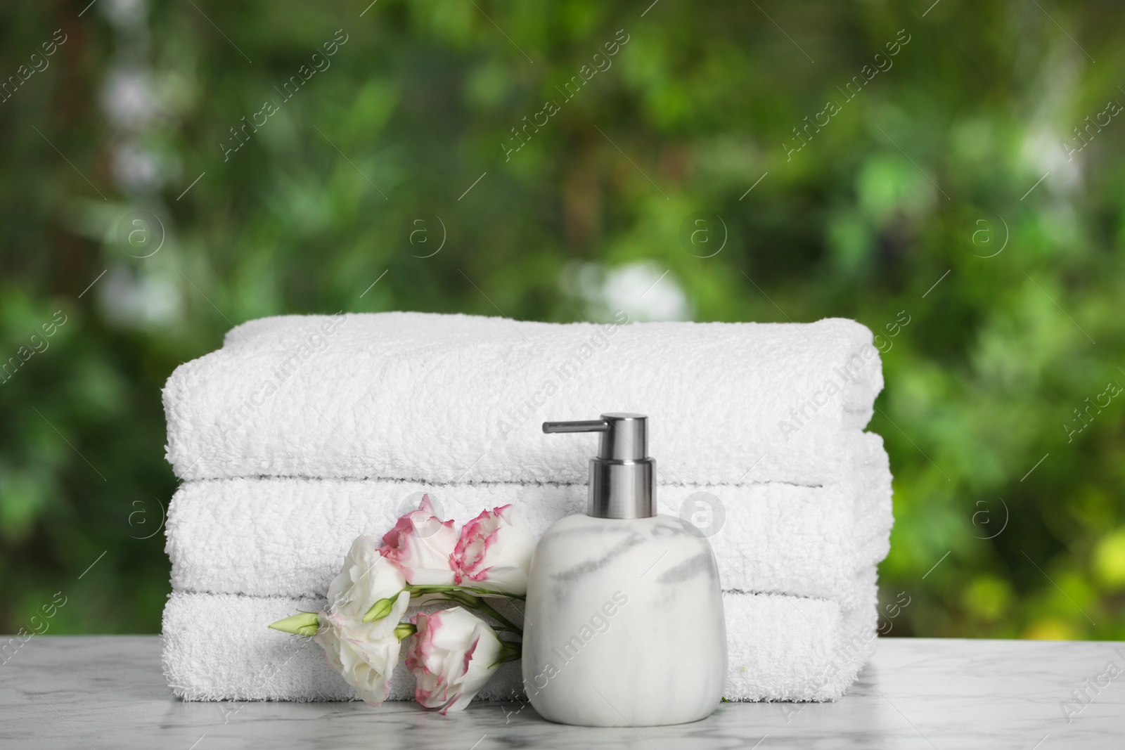 Photo of White soft towels, dispenser and flowers on marble table outdoors, closeup