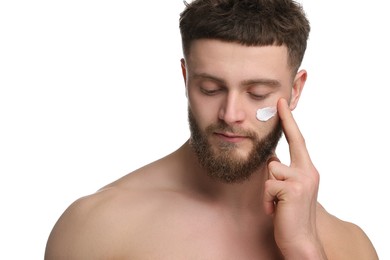 Handsome man applying moisturizing cream onto his face on white background