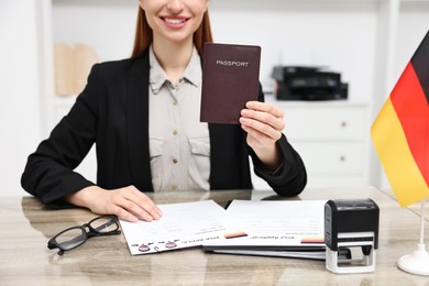 Immigration to Germany. Smiling embassy worker with passport and documents at wooden table in office, closeup
