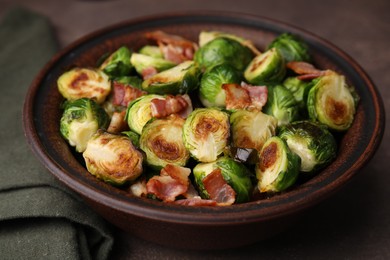 Photo of Delicious roasted Brussels sprouts and bacon in bowl on brown table, closeup