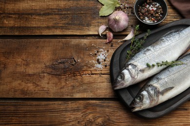 Photo of Sea bass fish and ingredients on wooden table, flat lay. Space for text