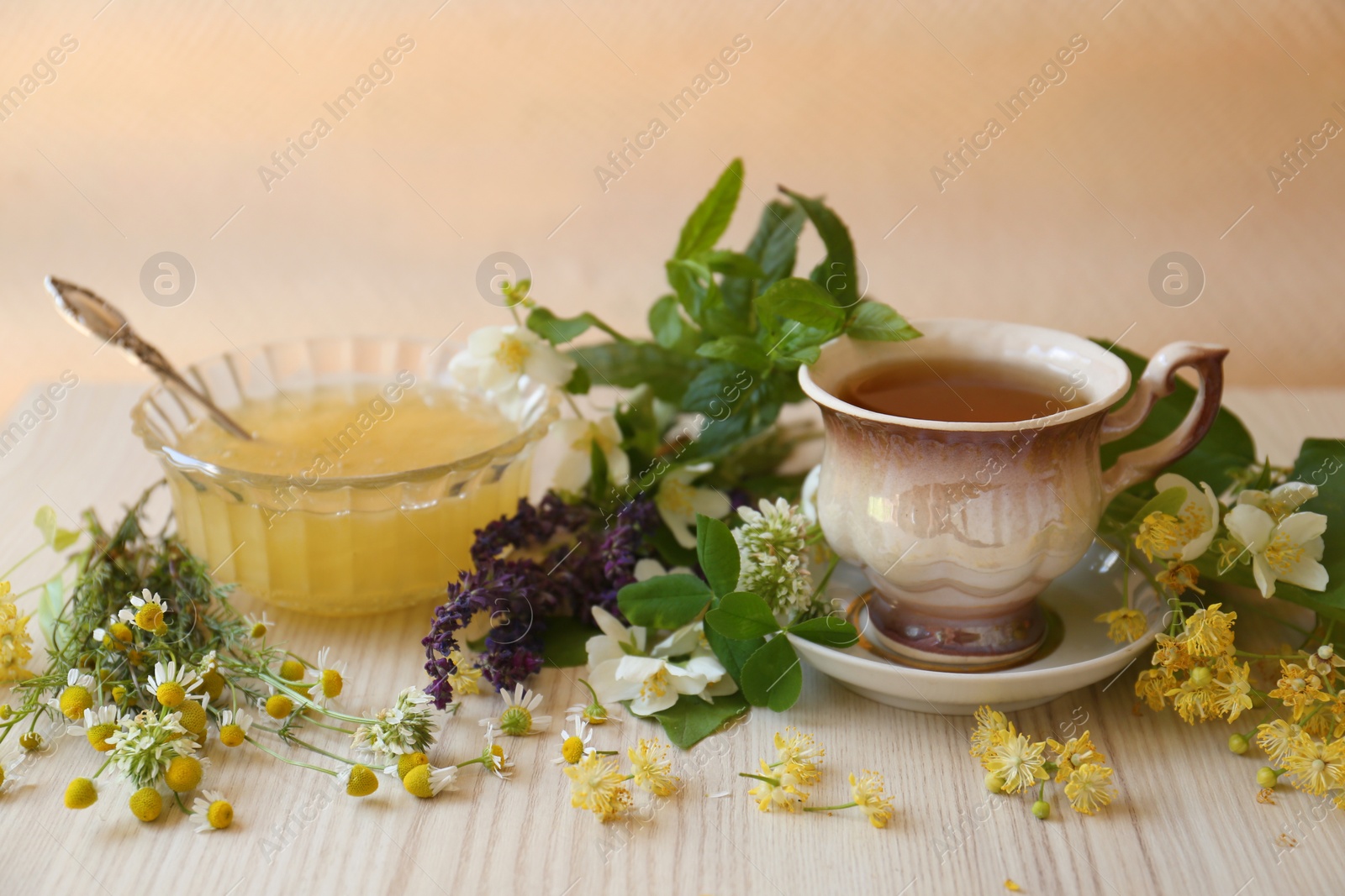 Photo of Cup of hot aromatic tea, honey and different fresh herbs on white wooden table