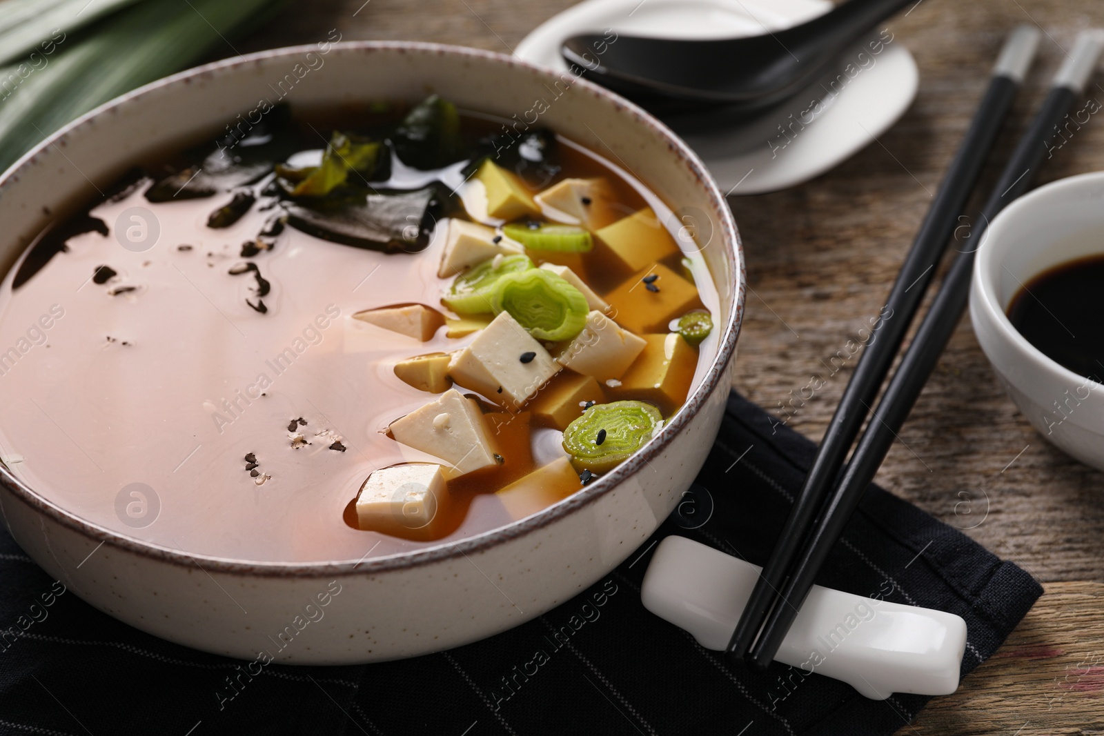 Photo of Bowl of delicious miso soup with tofu and chopsticks on wooden table, closeup