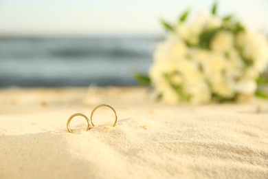 Photo of Beautiful gold wedding rings on sandy beach, closeup. Space for text