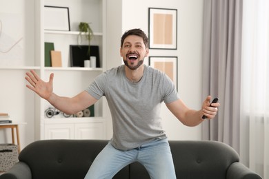 Photo of Emotional man holding remote controller and watching TV at home