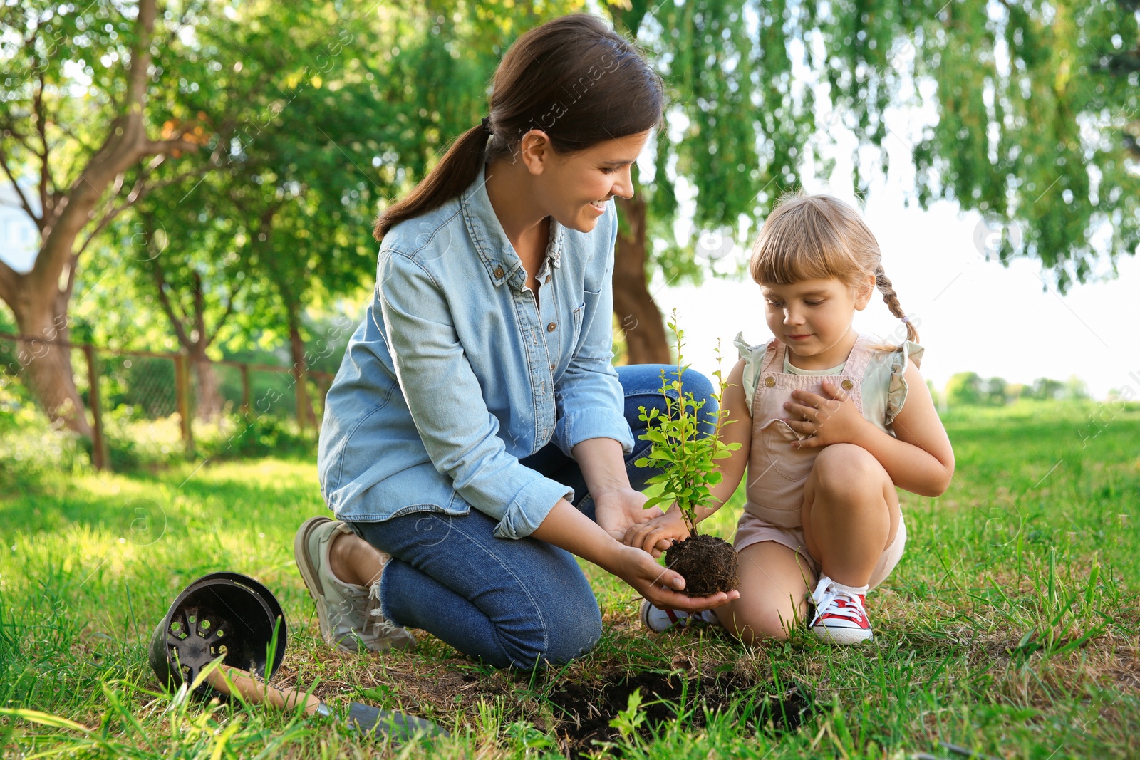 Photo of Mother and her daughter planting tree together in garden