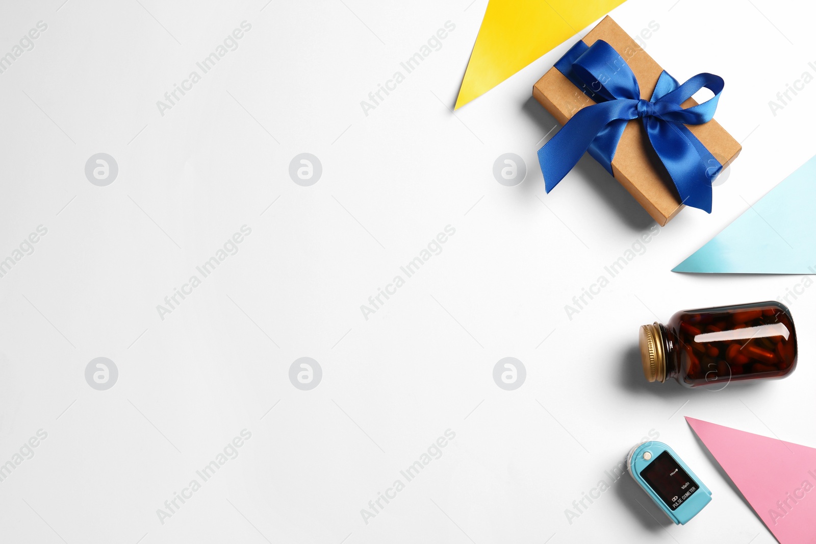 Photo of Fingertip pulse oximeter, bottle of pills and box on light background, flat lay with space for text. Medical gift
