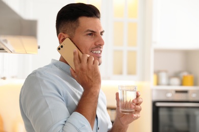 Photo of Man with glass of pure water talking on phone in kitchen