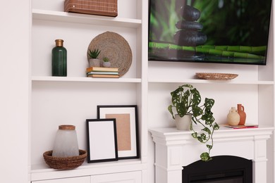 Photo of TV and shelves with different decor and houseplants in room. Interior design