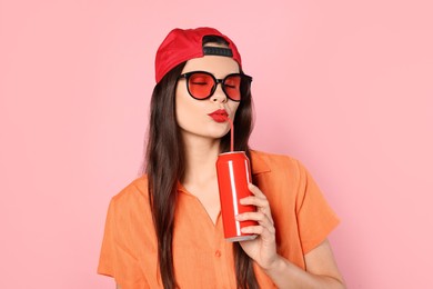 Photo of Beautiful young woman drinking from tin can on pink background