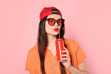 Beautiful young woman drinking from tin can on pink background