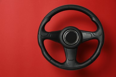 Photo of New black steering wheel on red background, space for text