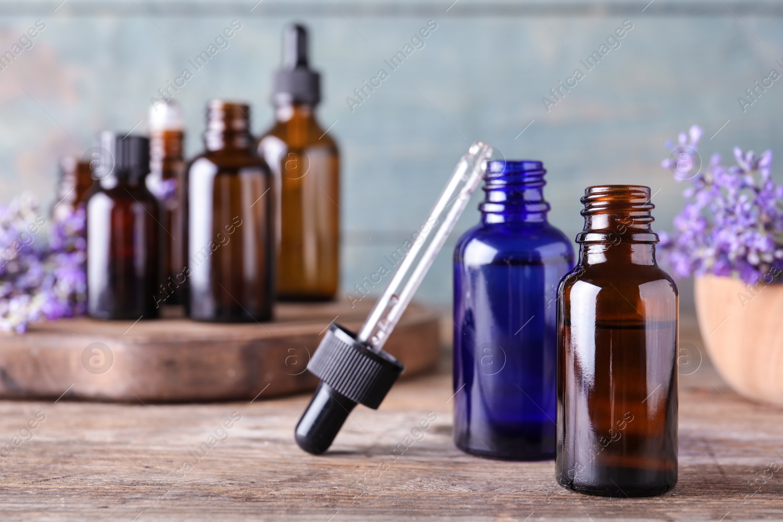 Photo of Bottles of lavender essential oil and flowers on wooden table against blue background