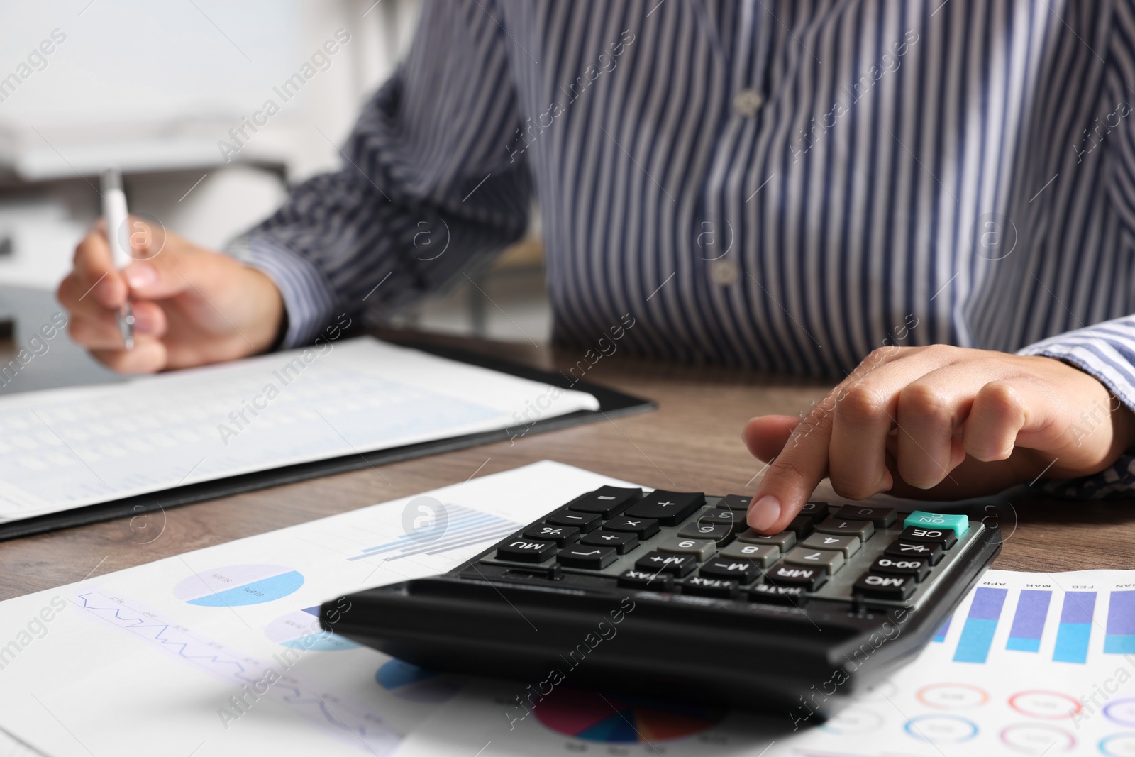 Photo of Woman using calculator while taking notes at table indoors, closeup