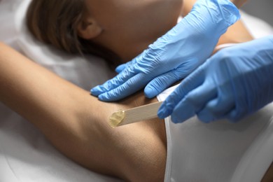 Photo of Young woman undergoing hair removal procedure of armpits with sugaring paste in salon, closeup