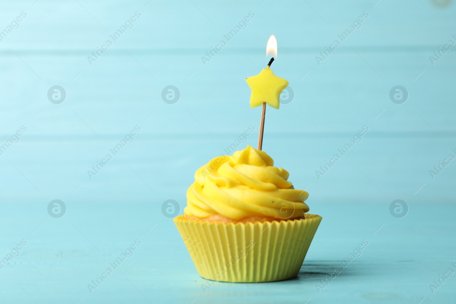 Photo of Delicious birthday cupcake with cream and burning candle on blue wooden background