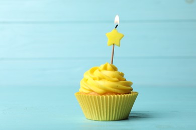 Delicious birthday cupcake with cream and burning candle on blue wooden background