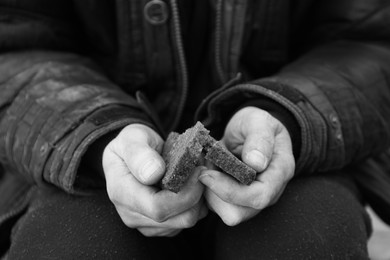 Photo of Poor homeless man holding piece of bread outdoors, closeup. Black and white effect