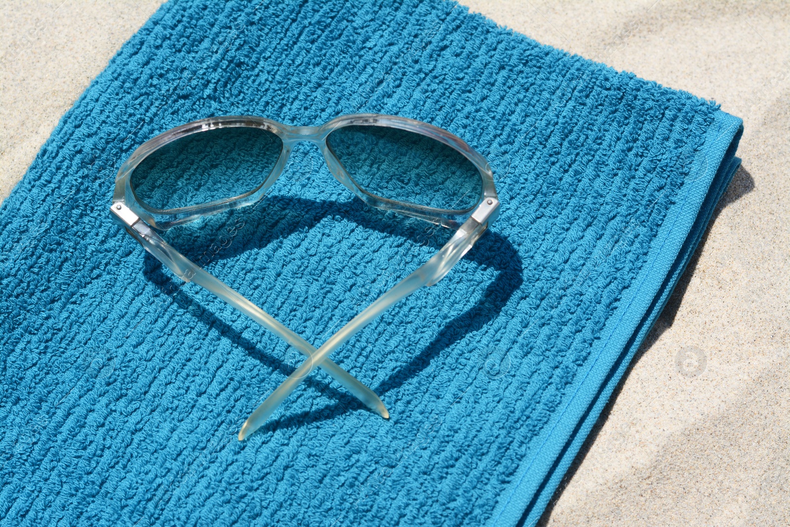 Photo of Soft blue towel and sunglasses on sandy beach, closeup