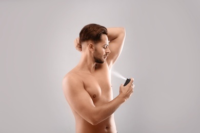 Young man using deodorant on gray background