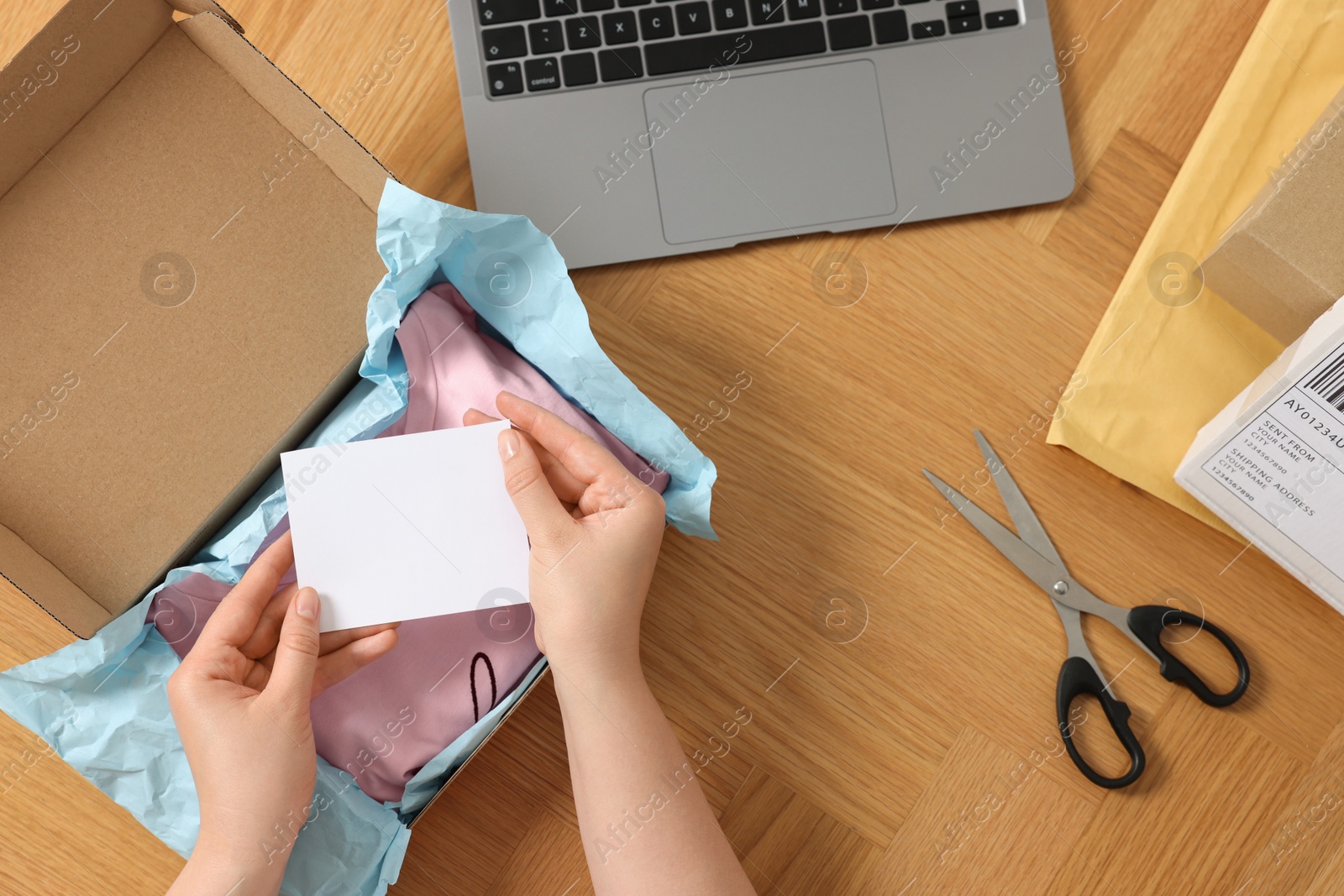Photo of Woman with paper card near parcel at wooden table, top view. Online store