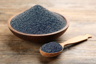 Photo of Poppy seeds in bowl and spoon on wooden table