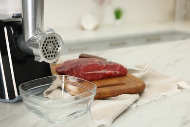 Photo of Electric meat grinder with beef on white table in kitchen, space for text