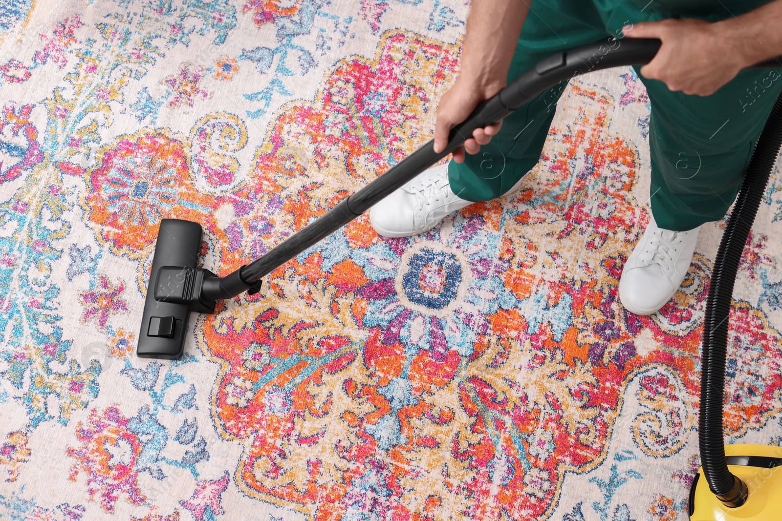 Photo of Dry cleaner's employee hoovering carpet with vacuum cleaner, above view