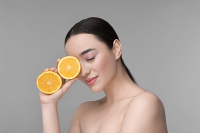Beautiful young woman with pieces of orange on grey background