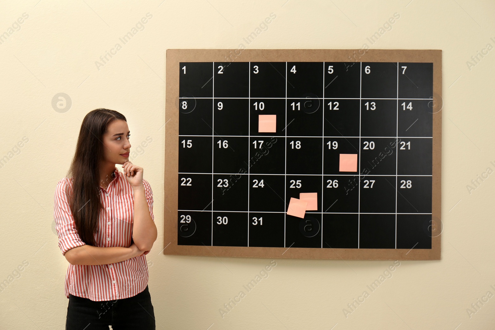 Photo of Young beautiful woman near board calendar  indoors