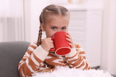 Photo of Cute girl drinking beverage from red ceramic mug at home