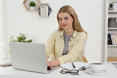 Photo of Home workplace. Woman working on laptop at white desk in room